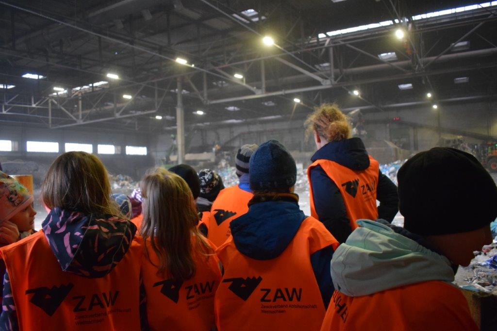 Mehrere Kinder betrachten die Arbeiten in einer Halle der Abfallwirtschaft.