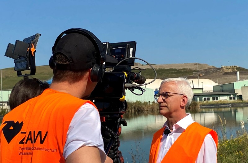 Der Geschäftsleiter des ZAW wird vor der Kulisse eines Teiches und der Mechanisch- biologischen Abfallbehandlung vom Dreh- Team des MDR mit Kamera und Mikrofon interviewt.