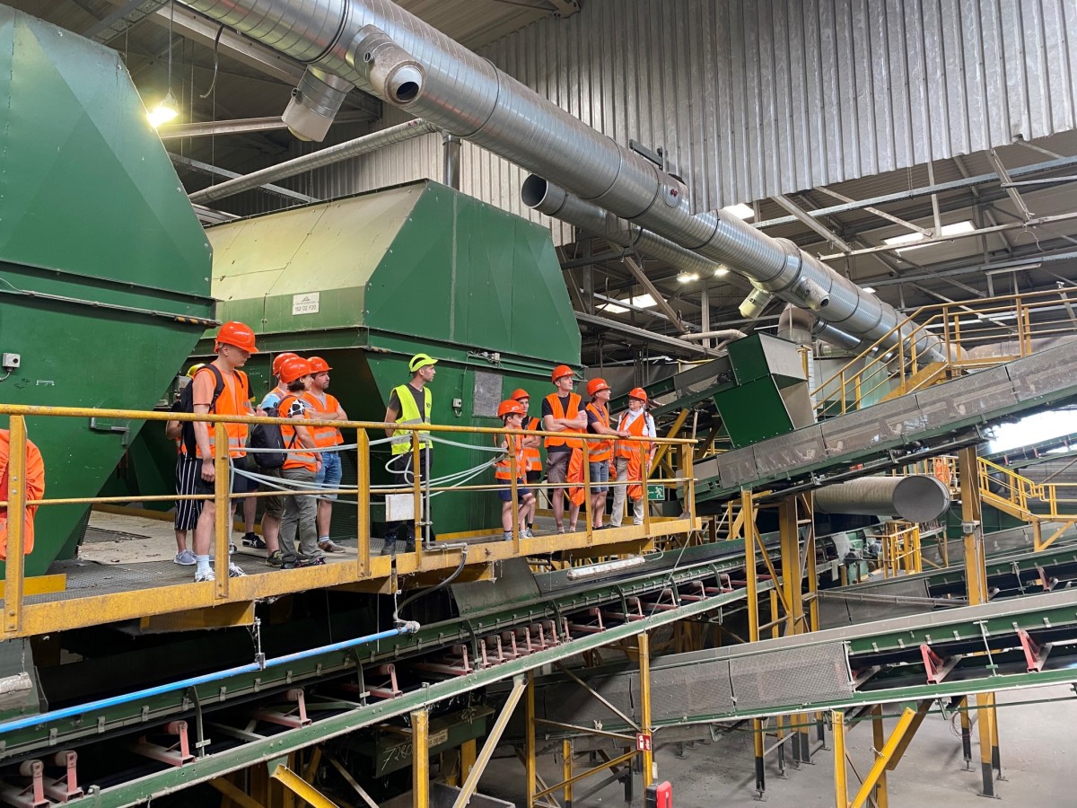 Personengruppe mit Arbeitsschutzbekleidung streht in einer Halle mit Förderbändern und verscheidenen Trennaggregaten.